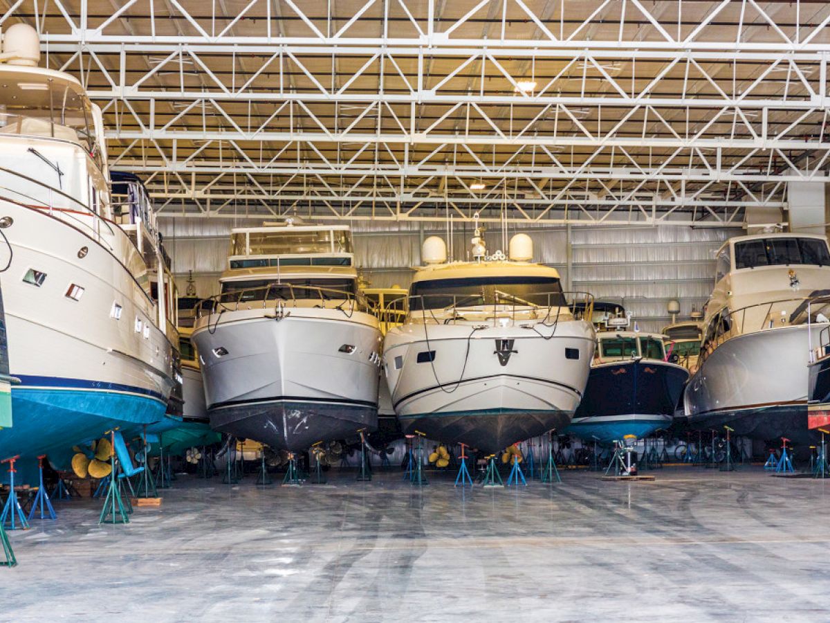 The image shows several large boats stored inside a spacious warehouse, supported by stands for maintenance or storage purposes.