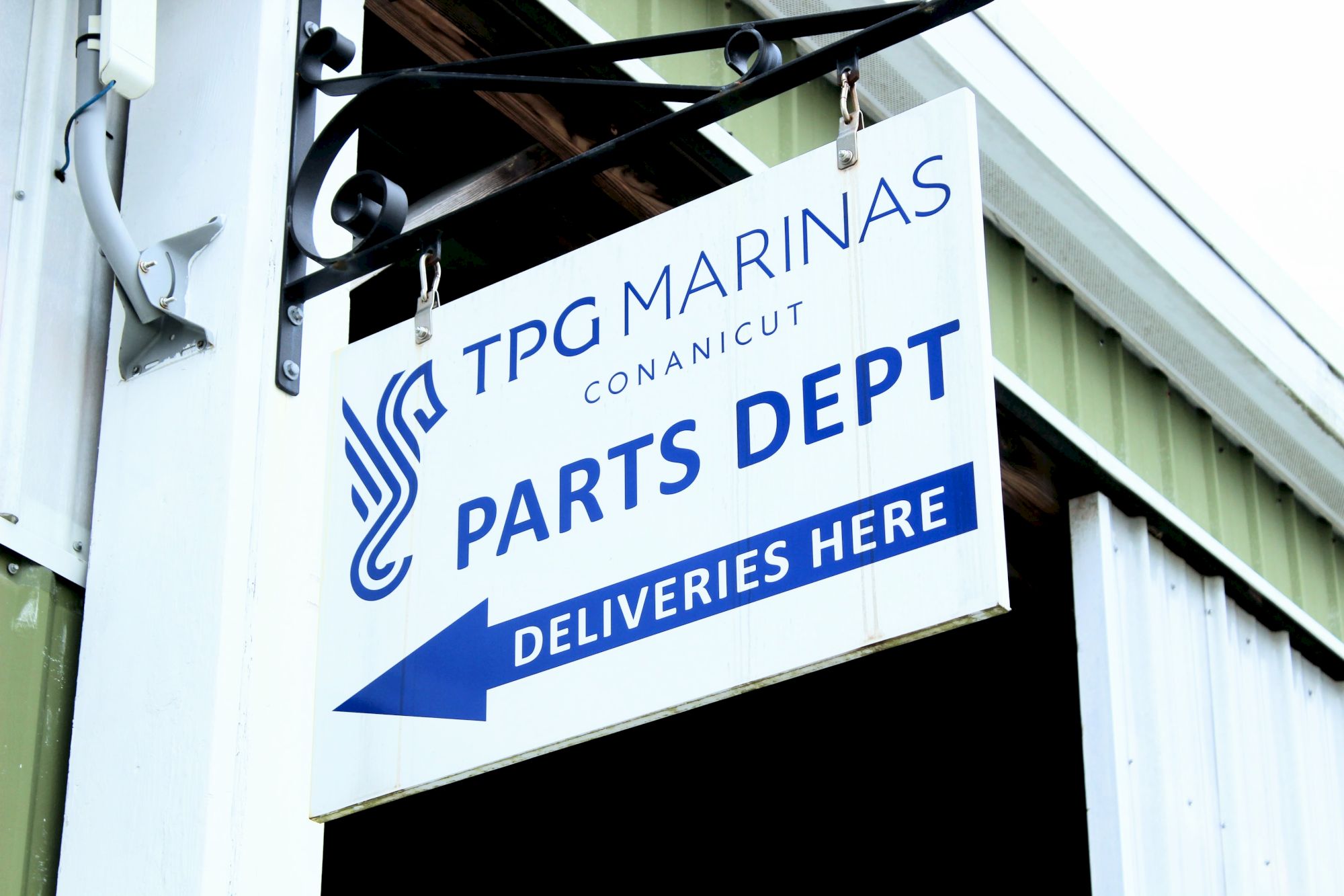 A sign for &ldquo;Parts Dept&rdquo; at TPG Marine Conanicut, indicating deliveries here; industrial building with blue and white signage.
