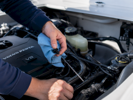 Mechanic&rsquo;s hands work in a Volvo engine bay, wiping a component while holding a screwdriver/tool.