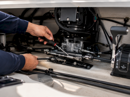 A mechanic&rsquo;s hands adjust a vehicle&rsquo;s engine components, using a red-tipped tool near the fuel/air system.