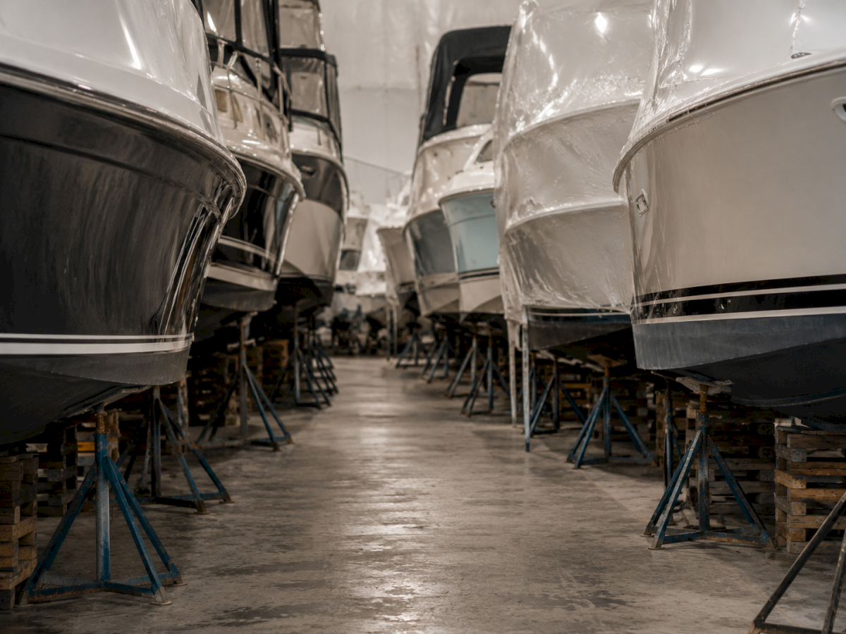 A workshop corridor with two rows of car bodies on stands, wrapped in plastic for painting or repair.