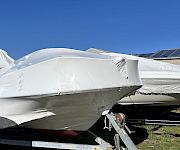 A boat-shaped aircraft hull wrapped in a white protective cover near solar panels under a clear blue sky.