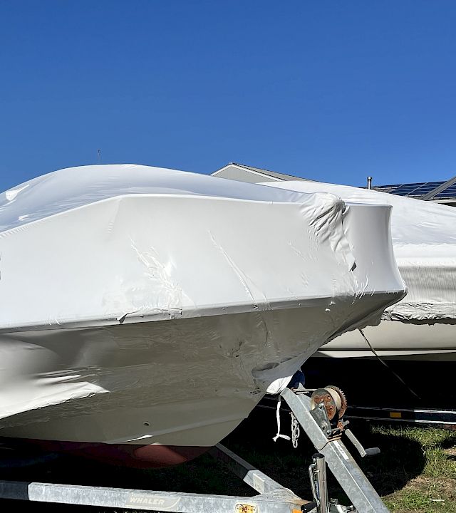 A boat-shaped aircraft hull wrapped in a white protective cover near solar panels under a clear blue sky.