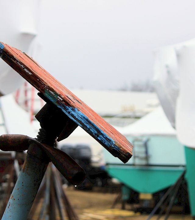 Close-up of a rusty, paint-chipped wooden plank on a metal stand in a cluttered workshop.