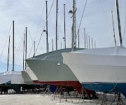 A row of sailboats on launch stands, covered with white protective tarps, at a dock/marina under a cloudy sky.