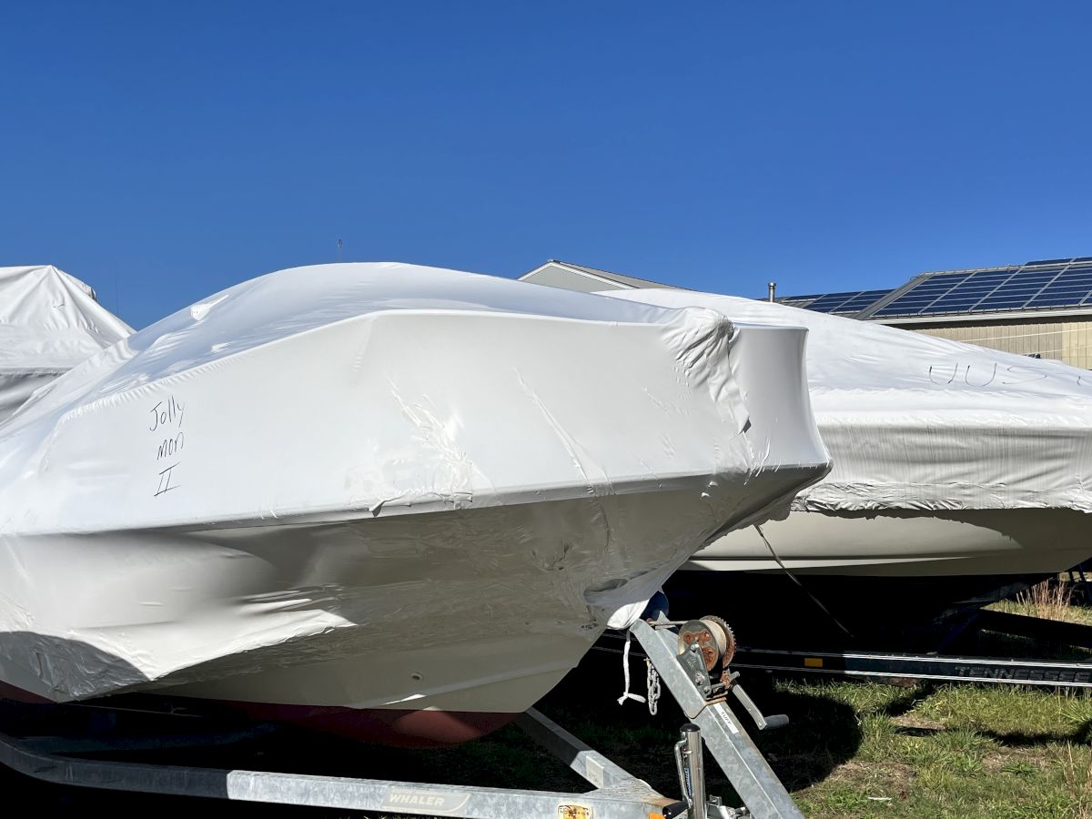 A small aircraft on a trailer, wrapped in white protective cover, with solar panels on a hangar under a clear blue sky.