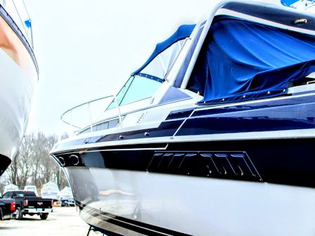 A luxury motorboat with a blue cover and white hull parked outdoors, surrounded by trucks and other boats.