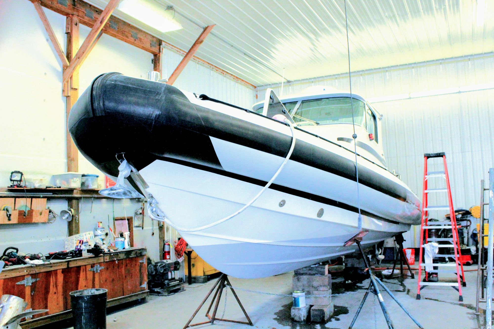 A white boat hull being worked on in a workshop, with rigging and tools visible around it.