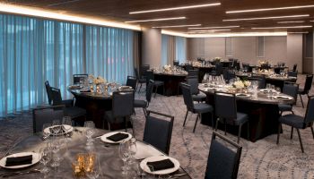 A modern banquet hall with round tables set for an event, featuring dark chairs, elegant table settings, and soft lighting from above.