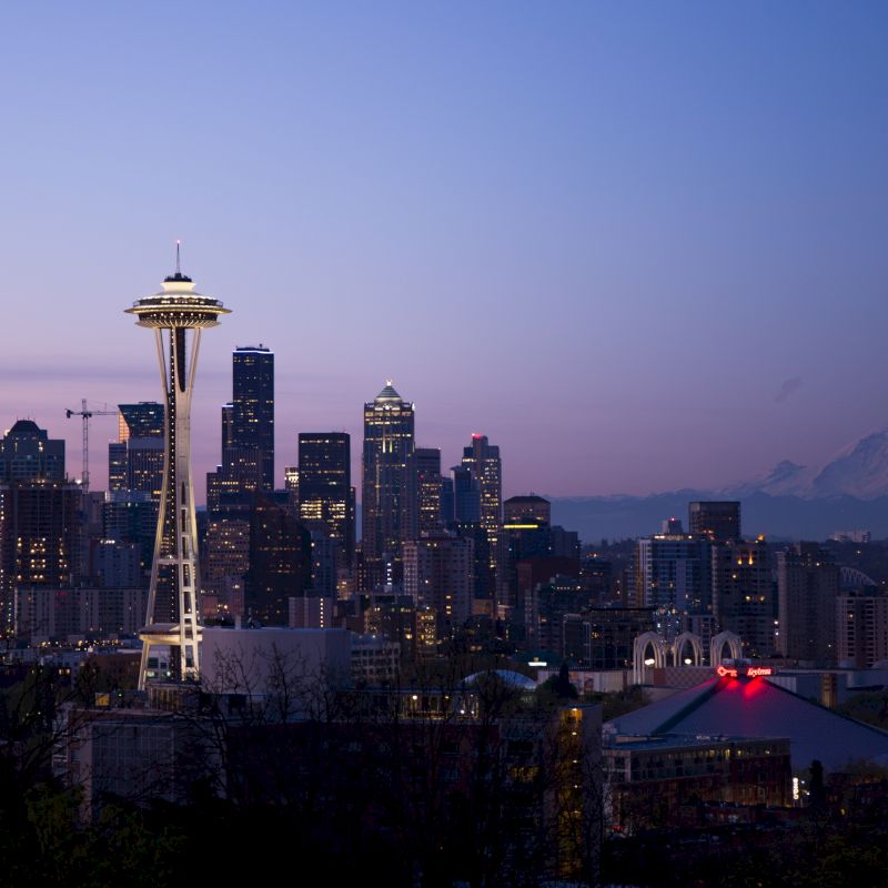 The image shows the skyline of Seattle at twilight, featuring the Space Needle, various buildings, and Mount Rainier in the background.