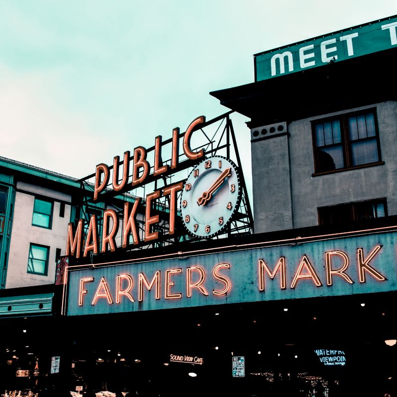 This image shows the infamous "Public Market" and "Farmers Market" neon signs at Pike Place Market in Seattle, known for its bustling atmosphere.