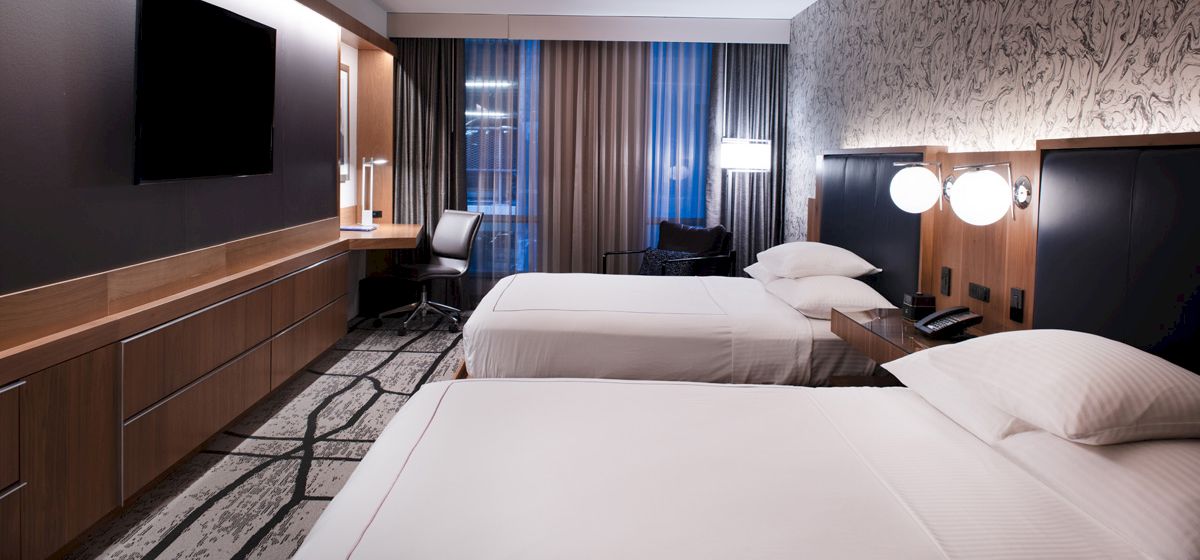 A modern hotel room with two beds, a TV, a desk, large windows, and contemporary lighting and decor ending the sentence.