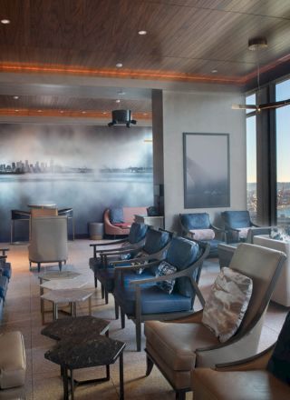 A modern lounge with plush seating, a mural on the back wall, and large windows offering a scenic view of the waterfront and a Ferris wheel.