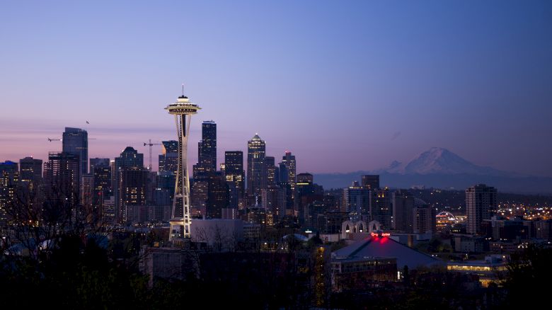 The image displays a twilight view of the Seattle skyline, featuring the Space Needle prominently and Mount Rainier in the background.
